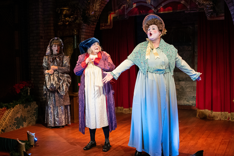 Maren Ward, center, as Ebenezer Scrooge in zAmya Theater Company’s “Scrooge in Rouge.”