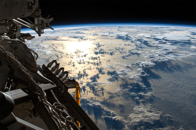 The sun's glint reflects off the Pacific Ocean shadowed by a line of cumulonimbus clouds as the International Space Station orbits about 253 miles above the Earth's surface.